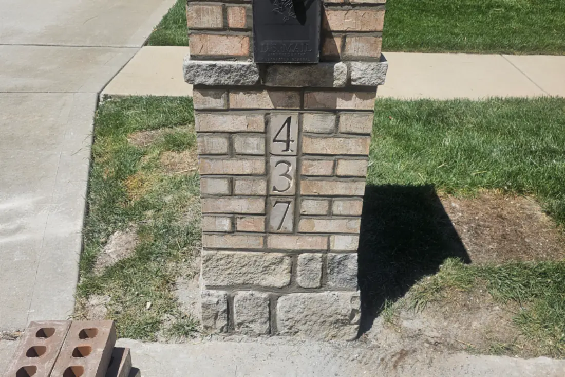 A mailbox pillar built in brick and cut stone with the house numbers set into the face, spare brick stacked alongside.